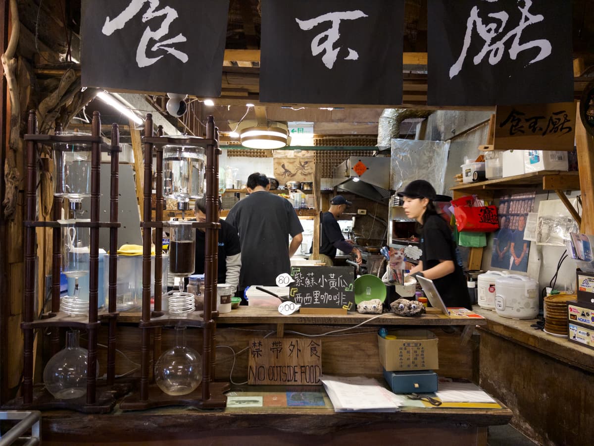 半開放廚房前的吧台，黑色暖簾上寫著「食不厭」，一旁是玻璃冰滴咖啡壺