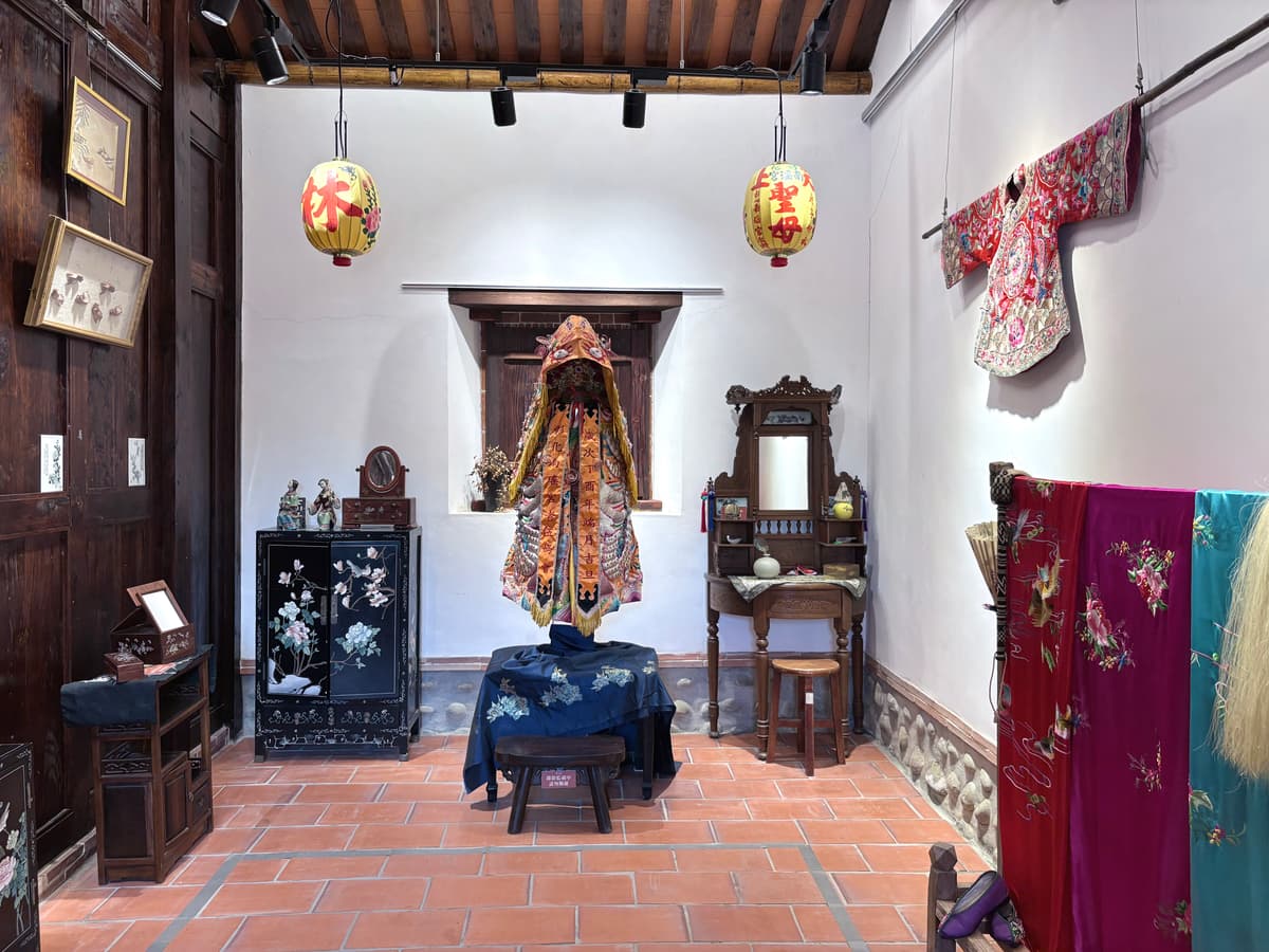 草厝展示空間,供著彰化南瑤宮媽祖金衣,兩側掛黃紙燈籠與清代花鳥刺繡
