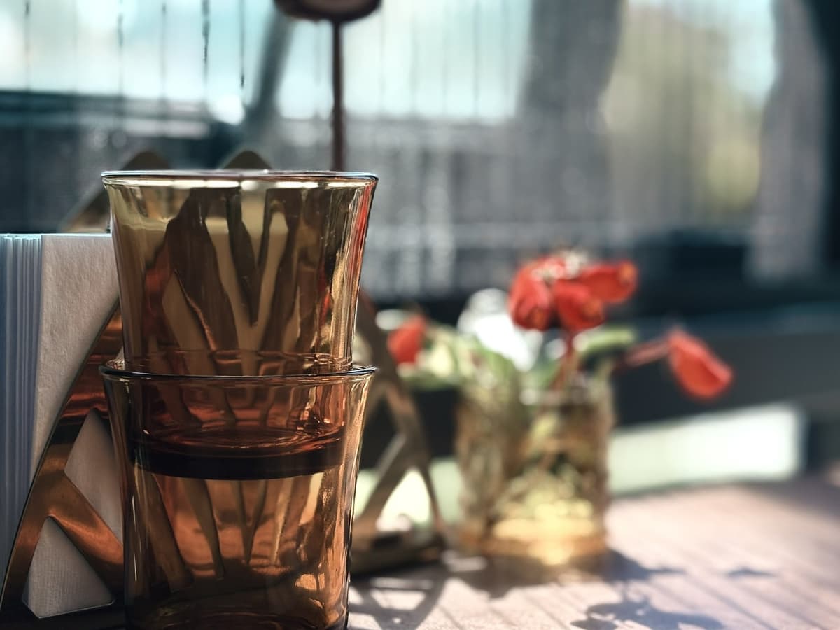 桌上疊放的銅色玻璃杯,旁邊一小瓶紅色小花