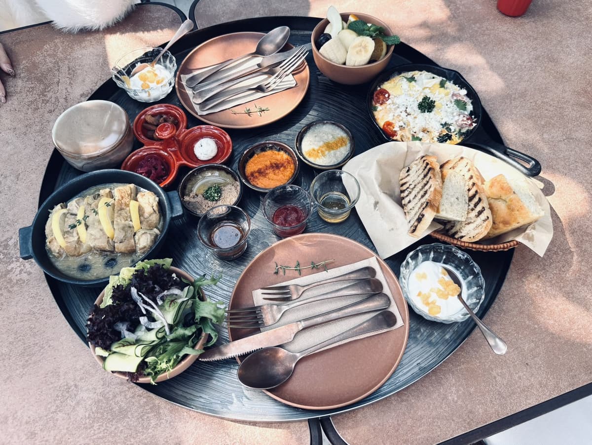 山里蒔花的地中海早餐盤,圓盤上有蕃茄燉蛋、香料烤雞腿、烤蔬菜、生菜碗、希臘優格與綜合麵包籃