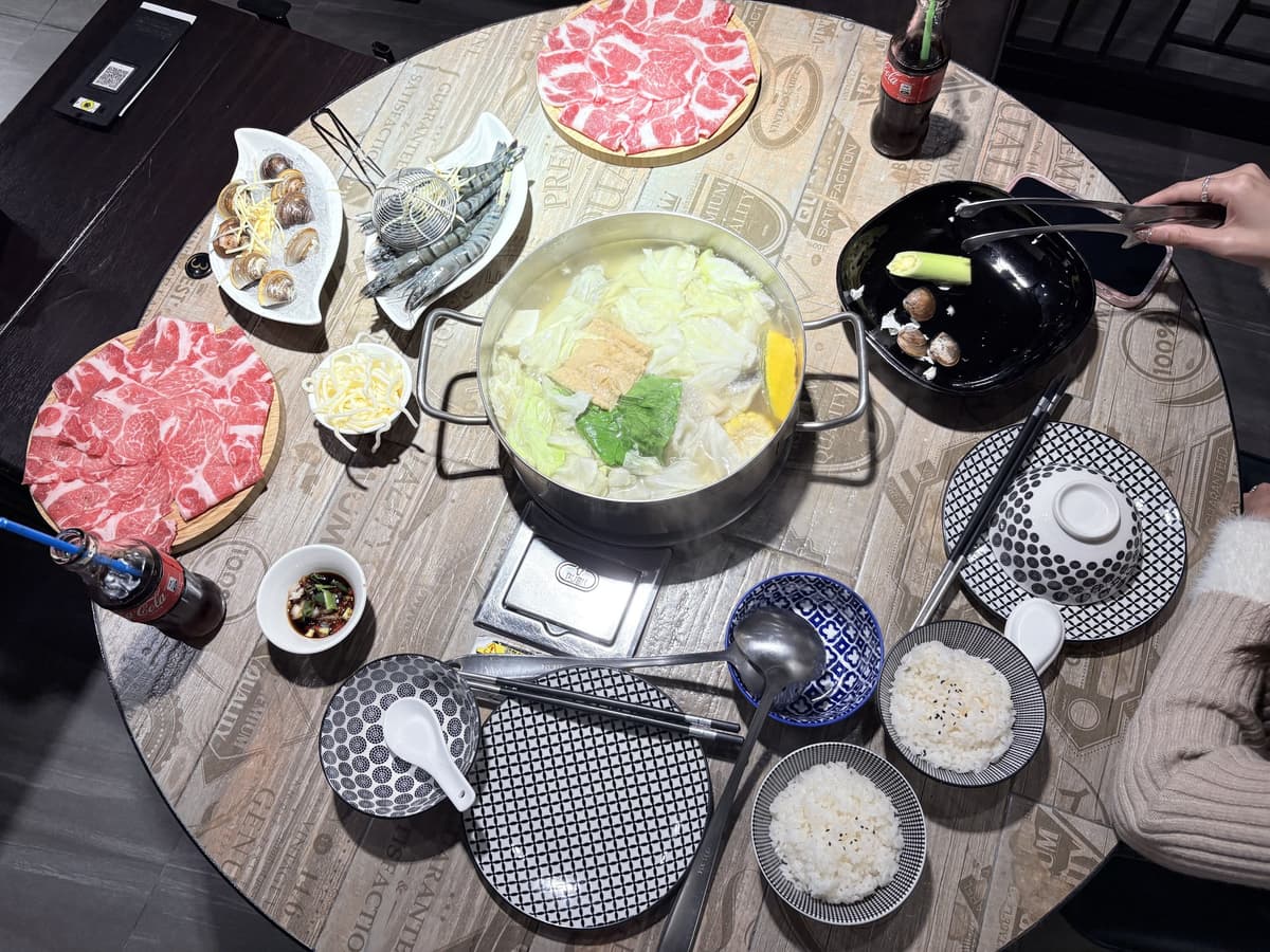 整桌火鍋俯瞰,中間是湯鍋,四周擺著肉盤、海鮮、菜盤與白飯